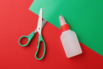 Bottle of glue, scissors and green paper on red background, flat lay