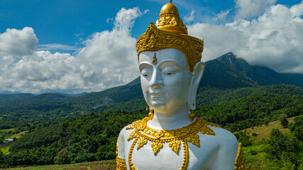 Close up the Tall Buddha Brahma Panyo statue standing tall in front of Doi Luang mountain, adorned...