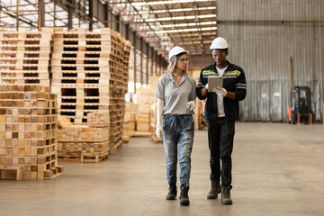 Team engineer manager wooden factory wearing safety uniform and hard hat working using tablet checking quality of wooden products furniture at workshop. Diverse ethnic worker hardwood warehouse.