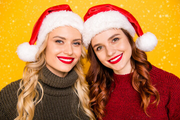 Pretty two ladies making holiday photos wear knitted pullovers and santa hats isolated yellow background