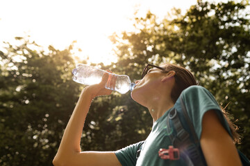 Active female drinking water while hiking outdoors in the forest,  body care, health concept 