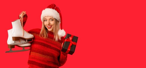 Beautiful young woman in Santa hat holding ice skates and Christmas gift box on red background with space for text