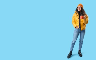 Fototapeta premium Happy young African-American woman with cup of hot mulled wine on blue background with space for text
