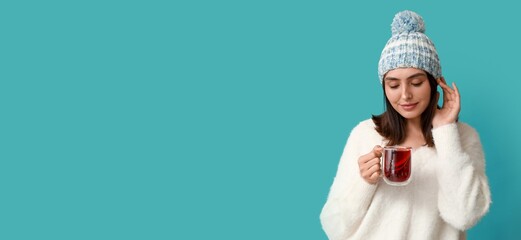 Beautiful young woman holding glass cup of hot mulled wine on blue background with space for text