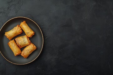 Delicious golden spring rolls arranged on a black plate with gold trim.