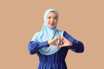 Beautiful Muslim woman with red ribbon showing heart gesture on brown background. AID awareness concept