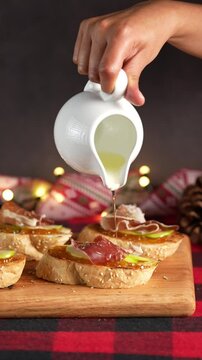 Vertical video, Christmas food, Spanish tapas, hands of a woman pour a little olive oil over a pintxo of Serrano ham, blurred background
