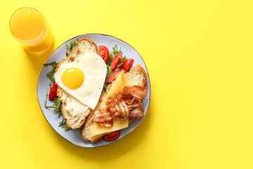 Plate with tasty fried egg, cut croissant, bacon, tomatoes and arugula on yellow background