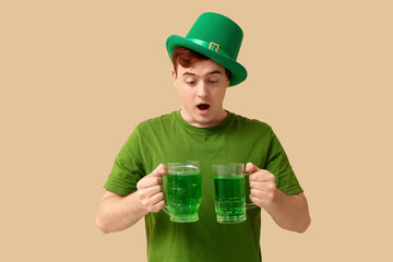 Shocked young man in leprechaun's hat with mugs of beer on beige background. St. Patrick's Day...