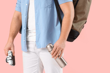 Male tourist with backpack, thermos and photo camera on pink background