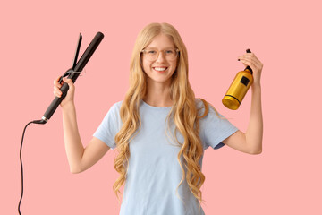 Beautiful young happy woman with curling iron and bottle of spray on pink background