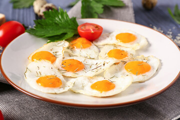 Plate with fried quail eggs, parsley and tomatoes on blue wooden background
