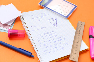 Notebook with calculator and school stationery on orange background