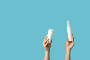 Female hands with plastic bottles of cosmetic products on blue background