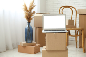 Blank laptop on moving boxes in light room, closeup