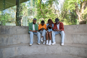Phone addiction. Immersed in smartphones African American friends sit together outside university...