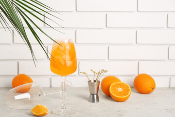 Glass of Aperol spritz cocktail with palm leaf and oranges on white table