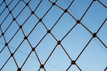 Fototapeta premium A close-up view of a rope net against a clear blue sky, showcasing the intricate knots and symmetrical grid pattern. The minimalist design emphasizes structure and simplicity in outdoor settings