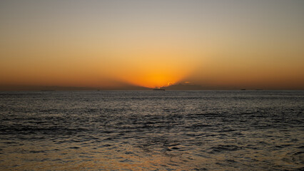 Obraz premium Golden sunrise over the ocean with dramatic clouds and calm waves, creating a peaceful seascape and warm morning glow.