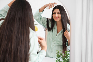 Fototapeta premium Young pregnant woman applying hair care product near mirror in bathroom