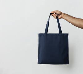 A hand is holding a blue tote bag. The bag is empty and has a simple design