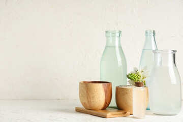 Bottles of natural rice water, grains and flower on light background