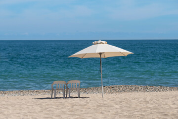 Sun umbrella and two chairs at empty white sand beach, turquoise ocean and blue sky in the background, no tourists around. South destination travel, holiday season concept.