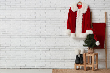 Obraz premium Hanger with Santa Claus costume, ladder with sack, fir tree and boots near white brick wall