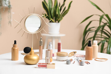 Different decorative cosmetics, makeup brushes and mirror on light table near color wall
