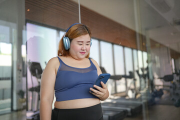 Fototapeta premium Obese asian woman Enjoy listening to music. Fat Female with headphones smart phone after workout at Gym