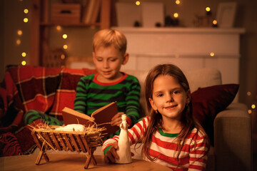 Little girl with angel and her brother reading Christmas story at home in evening