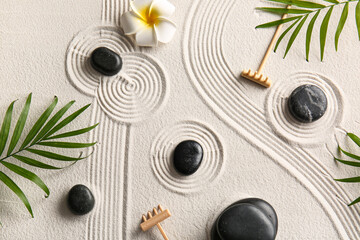 Black stones, small rakes and palm leaves on light sand with lines. Zen concept