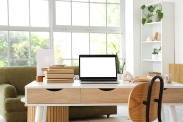 Blank laptop with books on programmer's desk in light living room