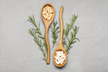 Wooden spoons with plant-based pills and rosemary on grey background