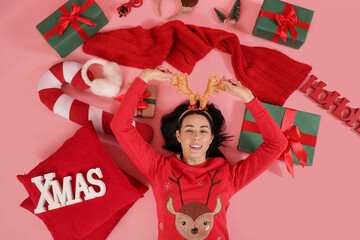 Pretty young woman with gift boxes and Christmas decorations lying on pink background