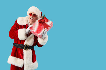 Young Santa Claus with Christmas gift on blue background