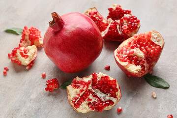 Fresh ripe pomegranates with leaves and seeds on grey background, closeup