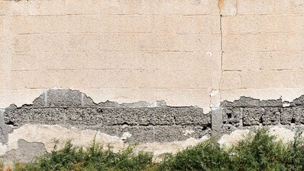 Peeling painted brick blocks concrete wall. Leaking rain cause the wall cracked. Water damaged the wall. Dirty grunge and rough surface with green grass.