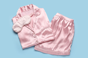 Stylish silk pajamas and sleeping mask on color background
