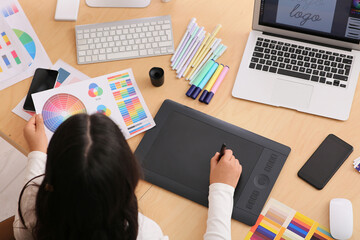 Young female graphic designer working with tablet and color palette at table in office