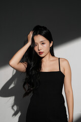 Naklejka premium 光と影の背景で撮影をした黒いドレスを着た若い女性のシックなポートレート