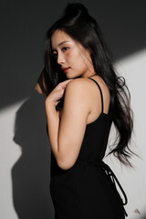 Naklejka premium 光と影の背景で撮影をした黒いドレスを着た若い女性のシックなポートレート