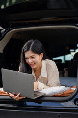 A woman parks her SUV camping car while camping in the morning and uses her laptop computer to work freelance.