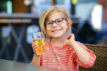 Adorable little girl having breakfast and drinking juice at resort restaurant. Happy preschool...