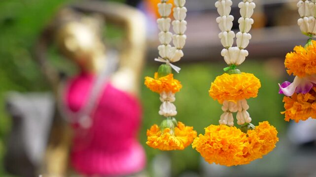 Close up of marigold flowers garland hanging and tilt focus change to the woman figurine statue near buddhist spirit house altar in Bangkok, Thailand
