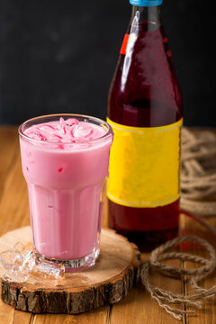 Rose milk sharbat with ice cube served in glass isolated wooden table closeup side view of arabic cold drink