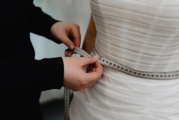 Naklejka premium wedding salon administrator measures bride waist at fitting in salon, cropped, no face, preparing to wedding, choose wedding dress concept