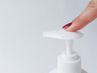 Hand pressing bottle dispenser button. Using liquid soap, shampoo dispenser. Applying moisturizer to hands.