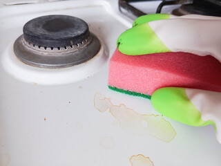 Hand in rubber glove washes dirty gas stove. Washing stains on kitchen stove with sponge. Background. Kitchen cleaning. Cleaning.