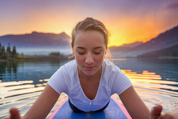 Fototapeta premium Young woman doing yoga on a SUP board at sunrise, fitness lifestyle